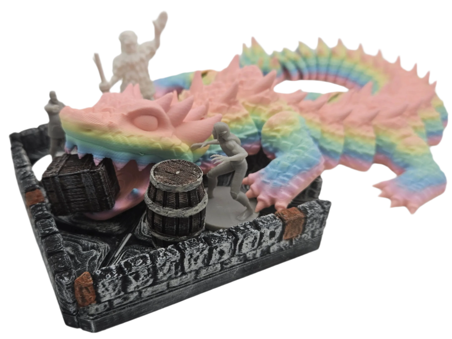 A rainbow dragon miniature is perched atop a dungeon wall set piece with miniatures, a barrel, and a treasure chest within.