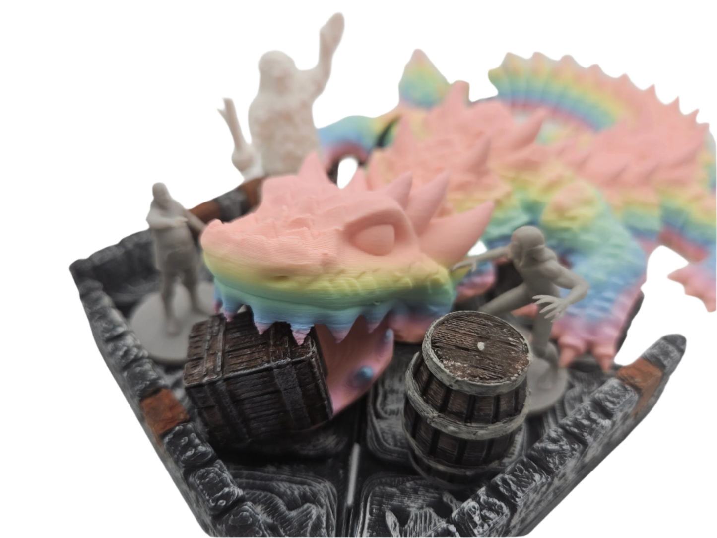 Miniatures populate a dungeon terrain: a pastel rainbow dragon head and wings, along with barrels and humanoid figures, are positioned in the setting.