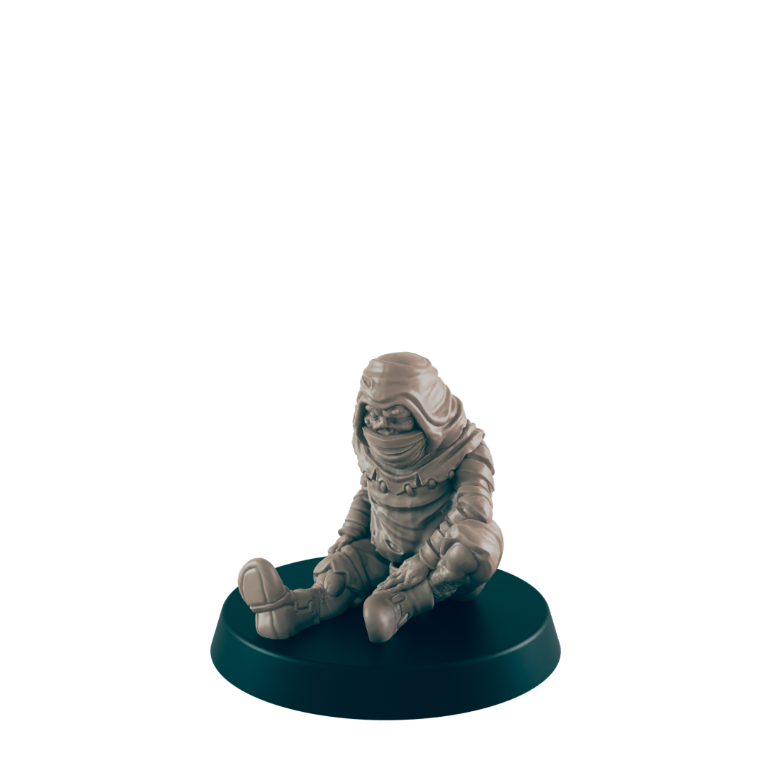 A small, hooded figurine sits on a dark circular base. It appears to be made of light brown clay or resin. The figurine is in a seated position with its legs crossed.