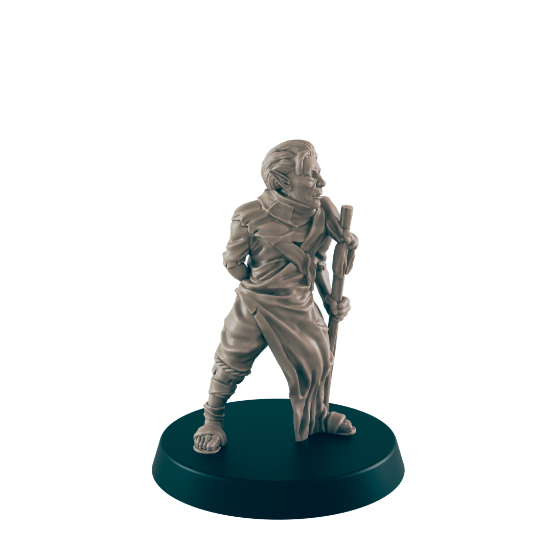 A miniature figurine of a robed humanoid stands holding a staff. The figure is light beige, positioned on a dark circular base.