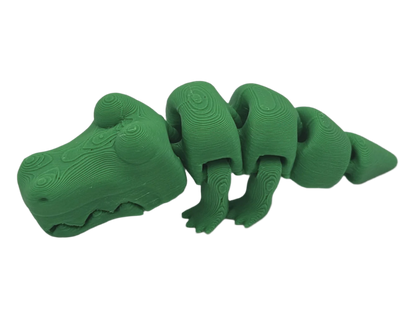 A green, articulated alligator toy rests on a black surface. Its segmented body features a faux-wood grain pattern, giving the toy a unique, textured appearance.