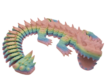 A rainbow-colored, articulated lizard is lying on a black surface. The lizard's tail curls upward and it opens its mouth.