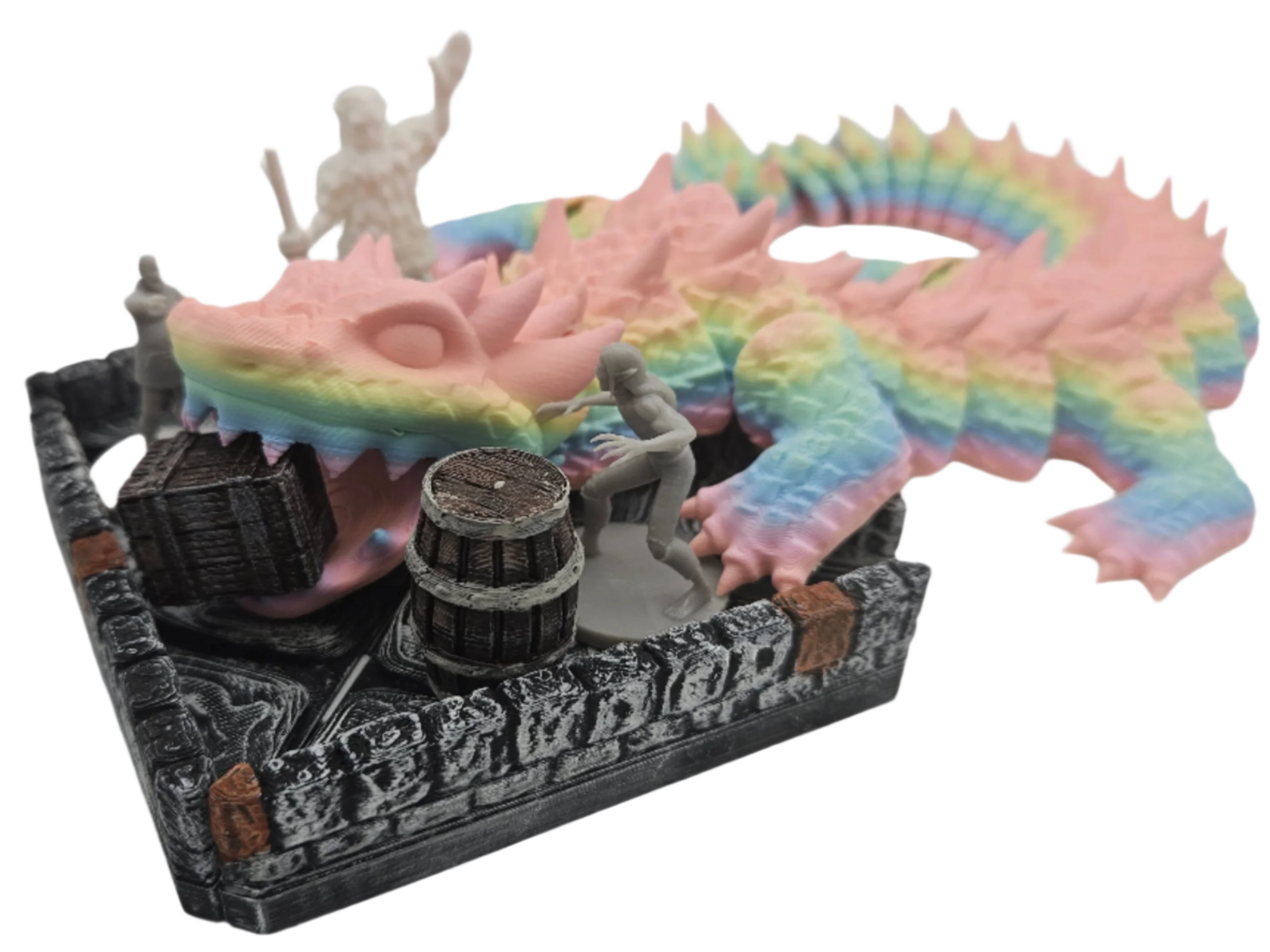 A rainbow dragon miniature is perched atop a dungeon wall set piece with miniatures, a barrel, and a treasure chest within.