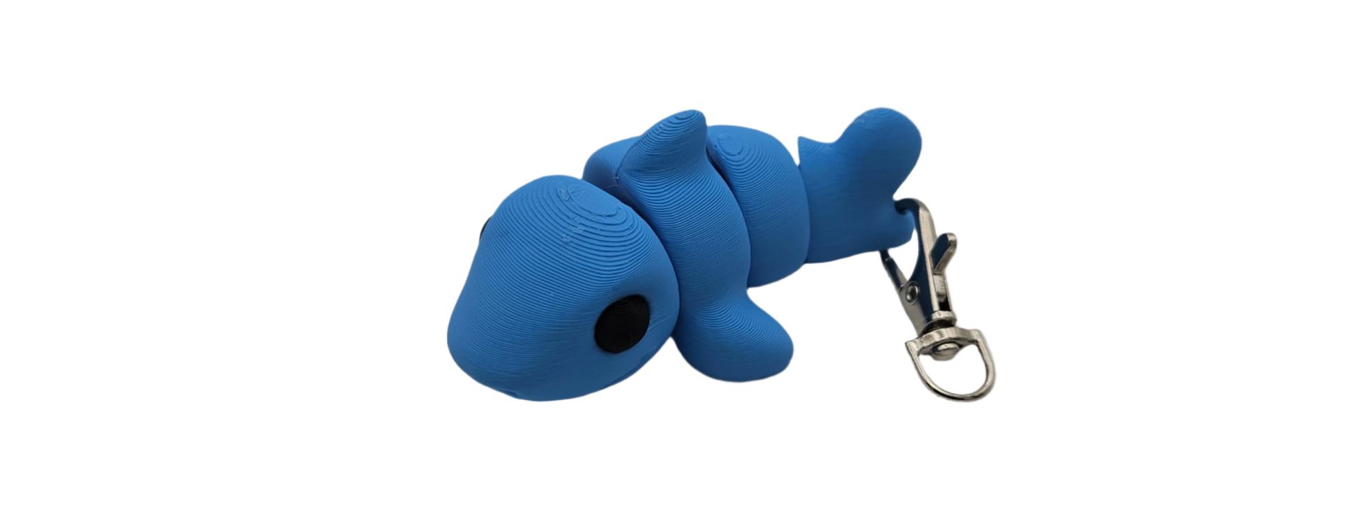 A blue fish-shaped toy keychain lies horizontally. The keychain is attached to the tail of the fish. It is isolated on a black background.
