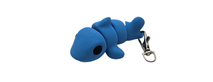 A blue fish-shaped toy keychain lies horizontally. The keychain is attached to the tail of the fish. It is isolated on a black background.