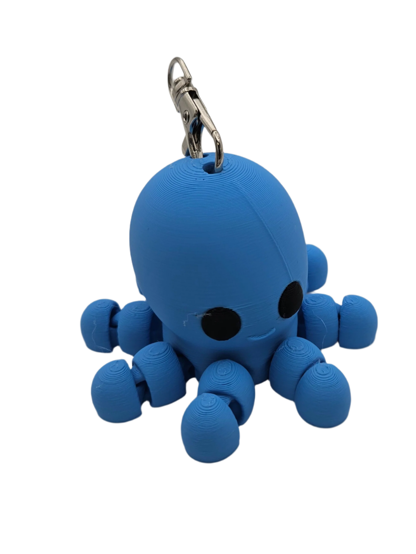 A small, blue, 3D-printed octopus keychain with large black eyes and a smiling mouth rests on a black surface. It has a metallic key ring attached to the top.