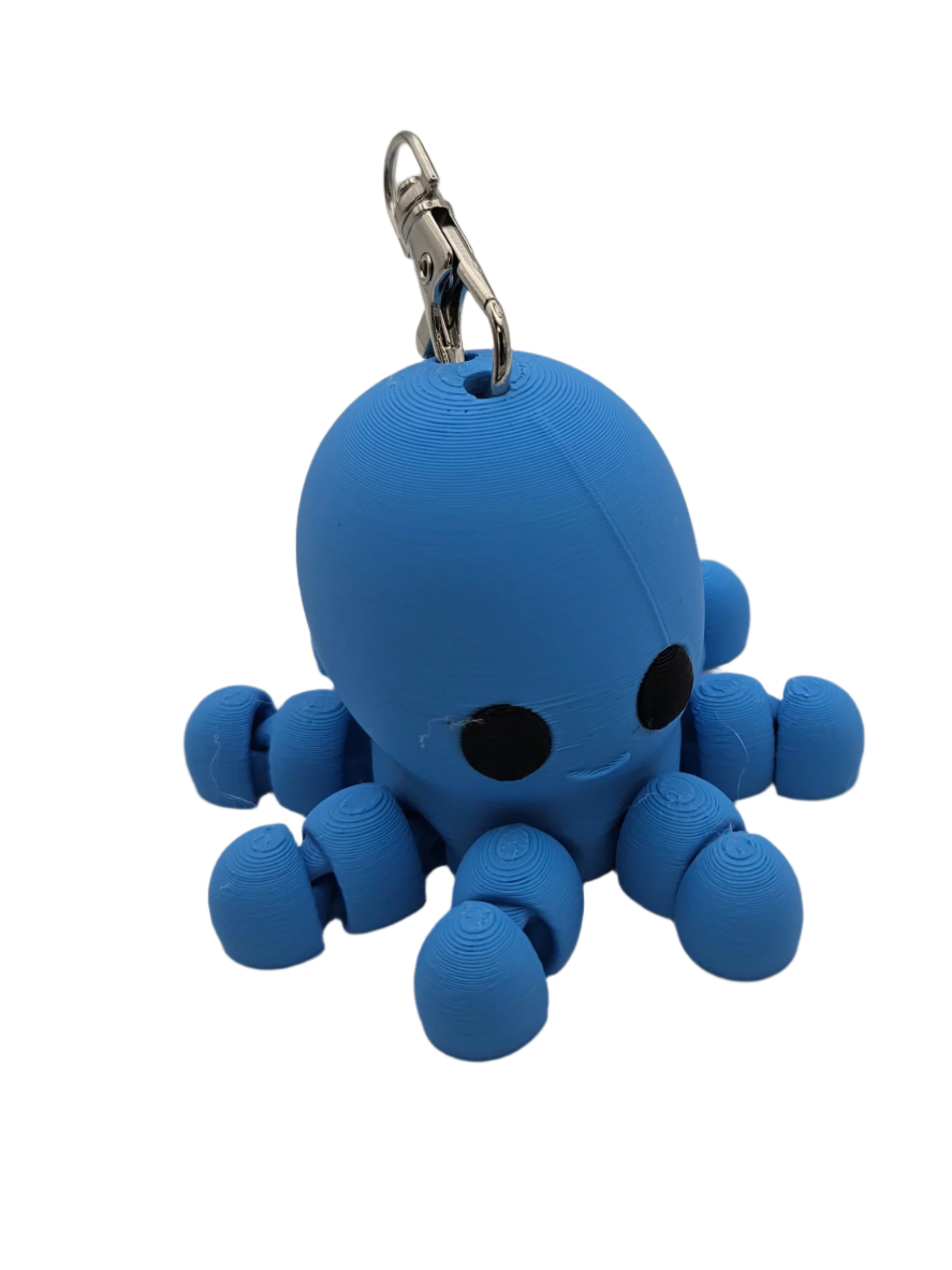 A small, blue, 3D-printed octopus keychain with large black eyes and a smiling mouth rests on a black surface. It has a metallic key ring attached to the top.