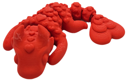 A red dragon figurine sits, showing its head, wings, and tail. The 3D-printed figure displays layer lines.