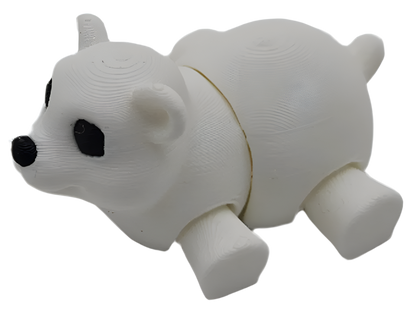 A 3D-printed white bear figure with black eyes and nose lays on a black surface. The bear's body is segmented at the midsection.