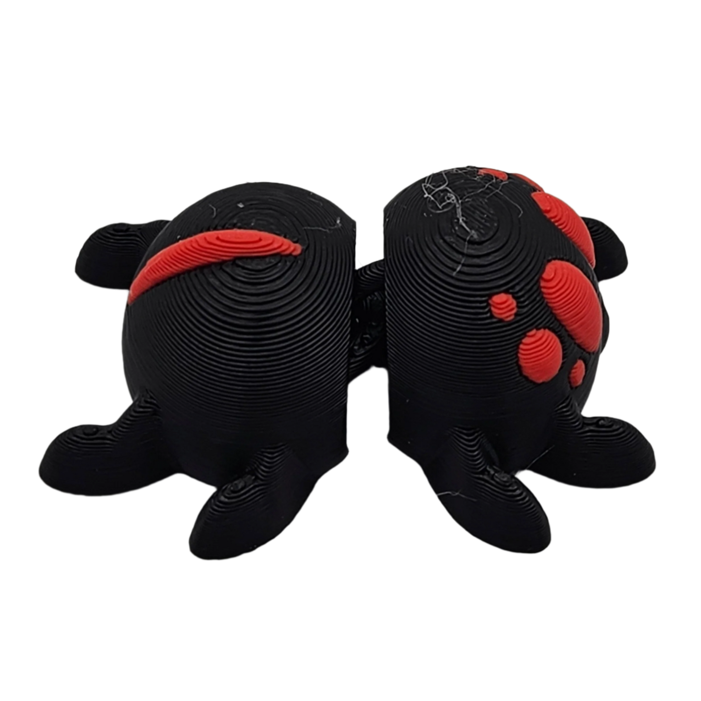 Two black, 3D-printed, semi-spherical bookends, each with four legs, stand next to each other. Red accents decorate each piece. They are set against a stark black backdrop.