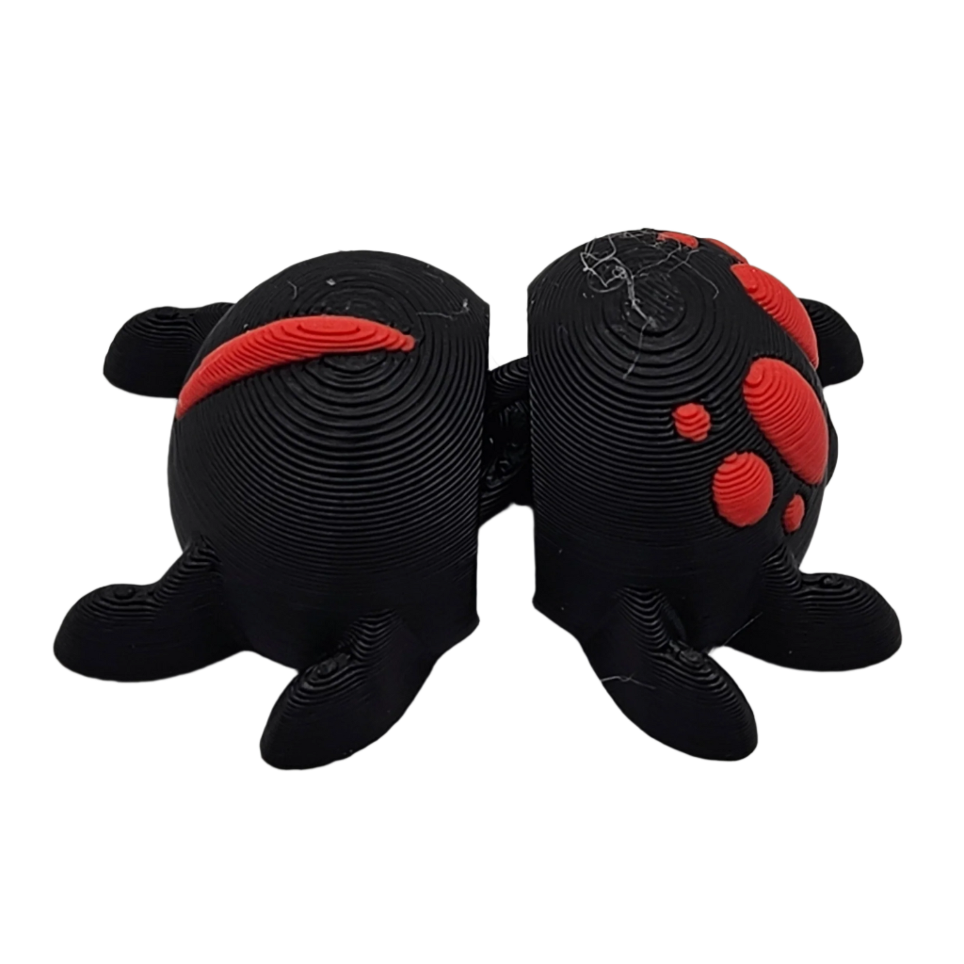 Two black, 3D-printed, semi-spherical bookends, each with four legs, stand next to each other. Red accents decorate each piece. They are set against a stark black backdrop.