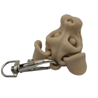 A tan, 3D-printed dog nose keychain with a silver metal clip is situated against a stark black background.