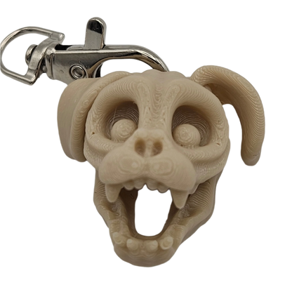 A stylized, beige dog skull keychain with a metal clip shows teeth in an open mouth. The head and ears are rounded, and its eyes are hollow.