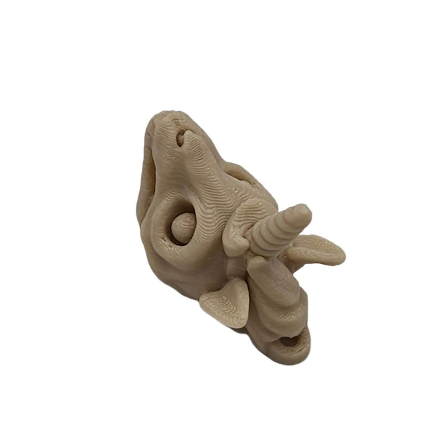 A beige, layered unicorn head faces upwards, its mane sculpted with horizontal lines, and a spiral horn extends outwards. It is set against a stark black background.