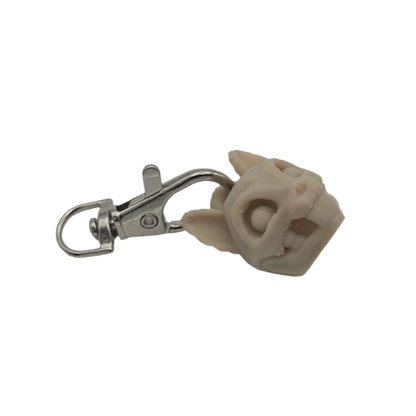 A pale cat skull keychain hangs horizontally against a black background, the skull's right side attached to a silver clasp.