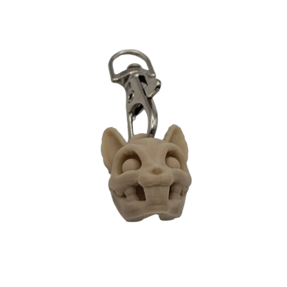 A cartoonish animal skull, made of pale tan material, dangles from a silver-colored metal clip in a black background.