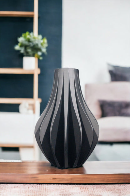 A decorative, gray vase sits centered on a wood tray. A navy wall with a plant on a shelf and a light-colored couch fill the blurred background.