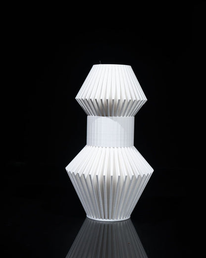 A white, vase-like object sits centered in a black space. The object is made of vertically ribbed pieces connected in a hourglass shape.
