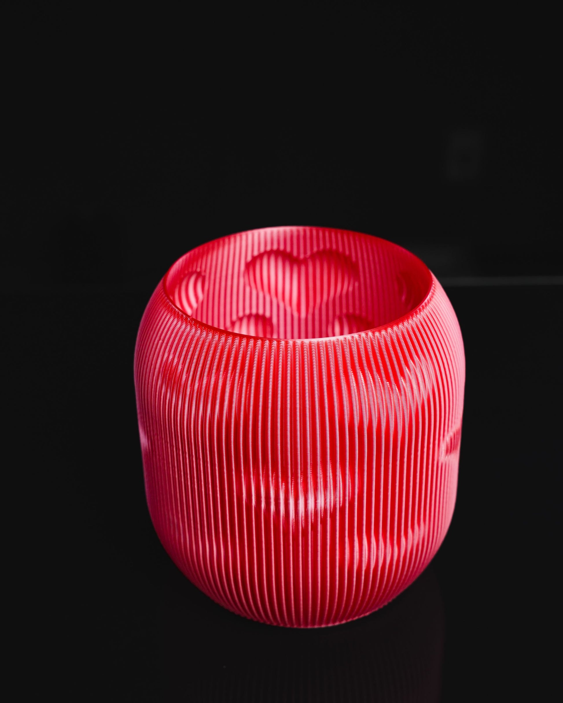 A red, spherical vase is on display against a black background. Its design features vertical ribs and heart-shaped cutouts near the top.
