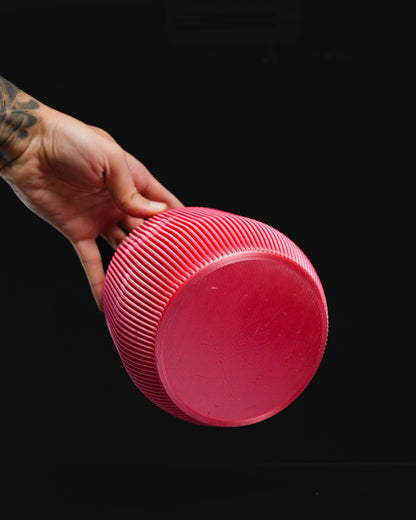 A tattooed hand holds a pink, spherical object with parallel ridges against a solid black background.