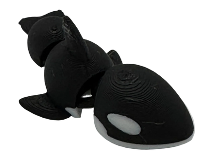 A textured, black and white 3D-printed orca model stands on a black background. It is segmented, with two connected body sections.