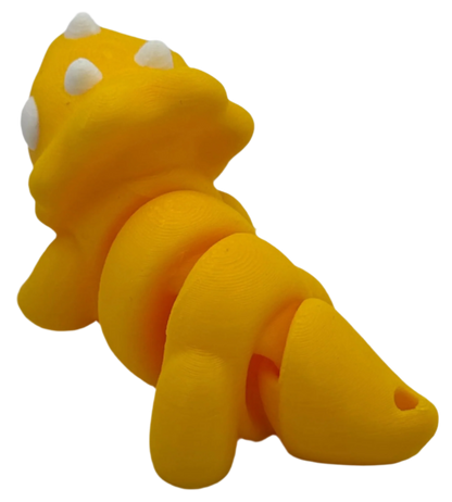 A yellow triceratops-like toy with white spots is displayed, its segmented body arching slightly, against a stark black background.
