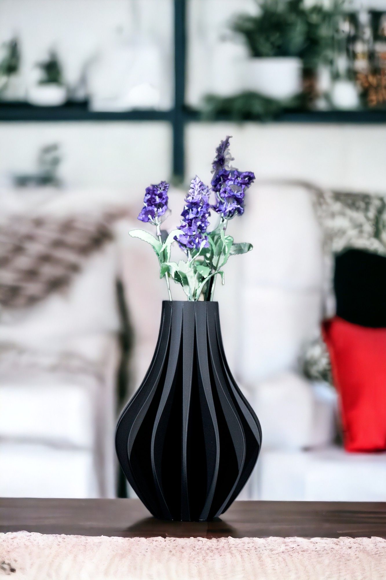 Flowers sit in a black, teardrop-shaped vase on a brown surface, set against a backdrop of living room decor.