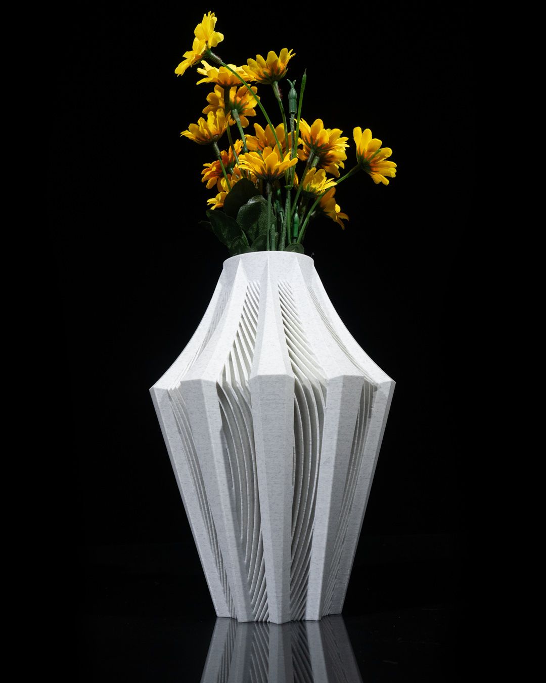 A white, intricately carved vase holds a bouquet of yellow flowers.  The vase sits on a reflective black surface.