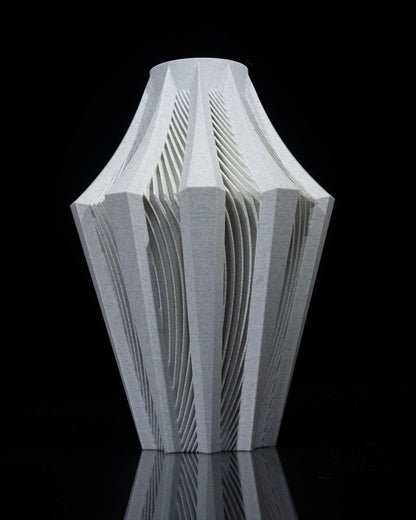 A light grey vase, featuring an intricately carved, pleated design, sits on a reflective black surface.