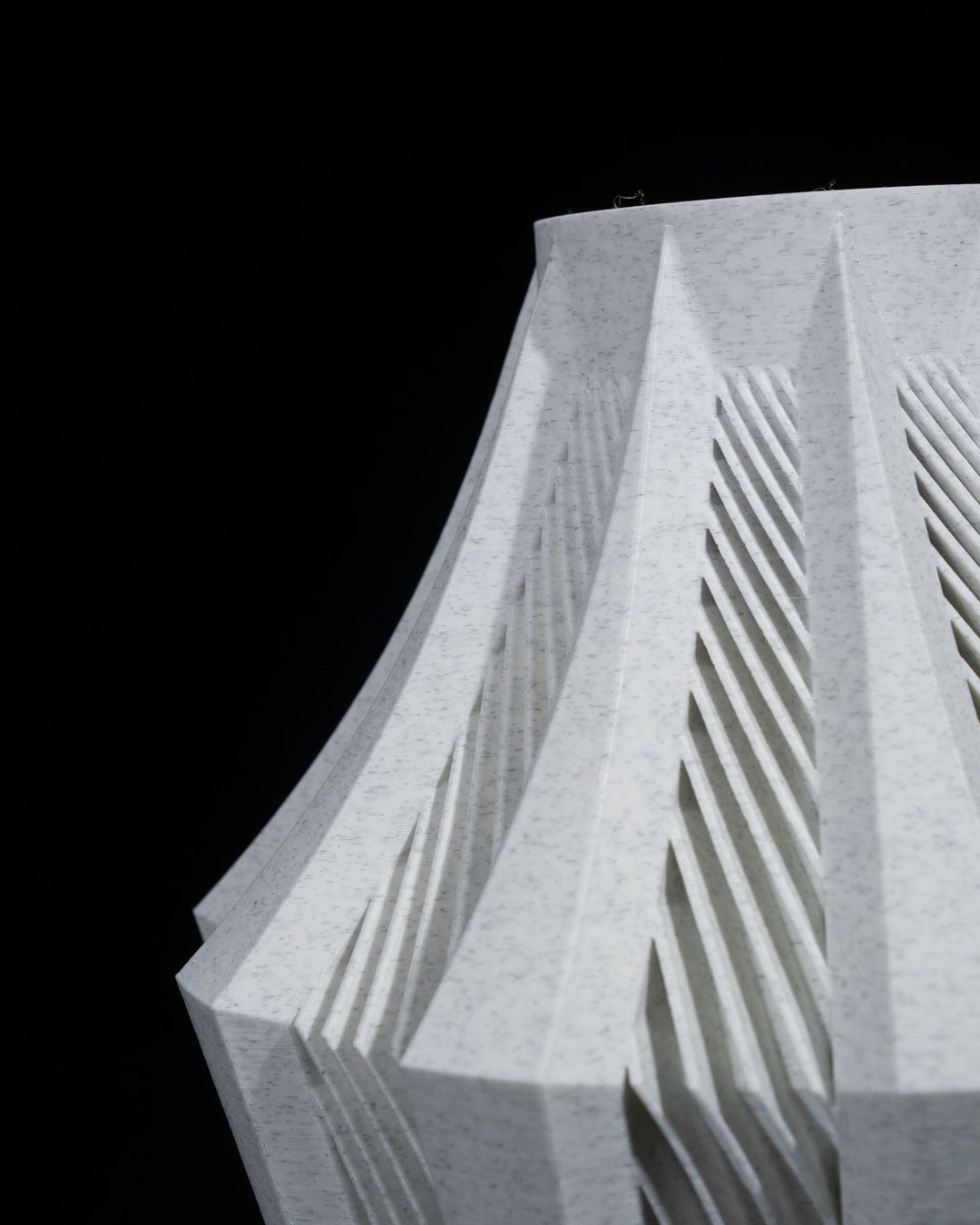 A light-grey, textured lampshade, featuring a geometric, pleated design, stands against a black background.
