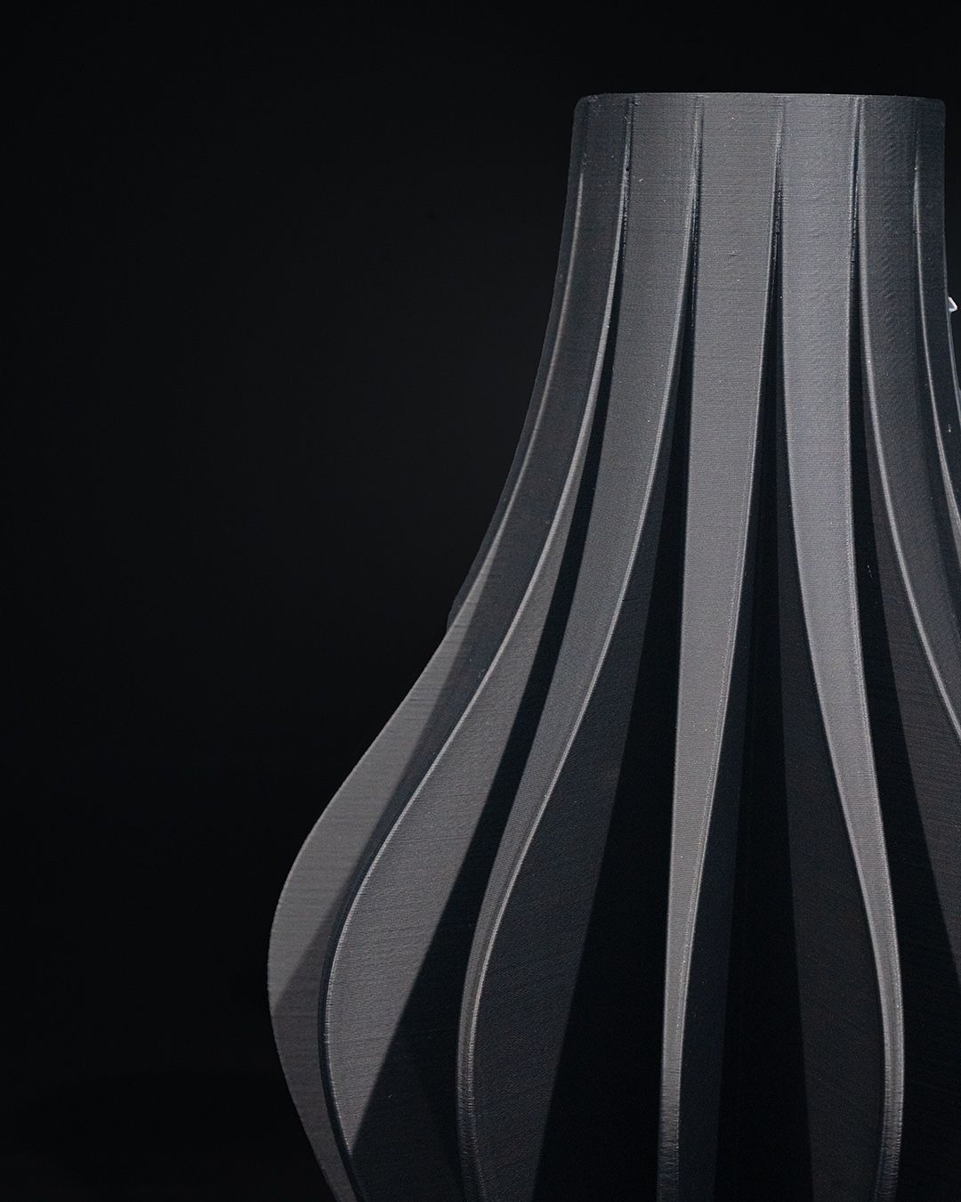 A vase with a fluted design stands against a black backdrop. Vertical fins curve outward from the base to the top.