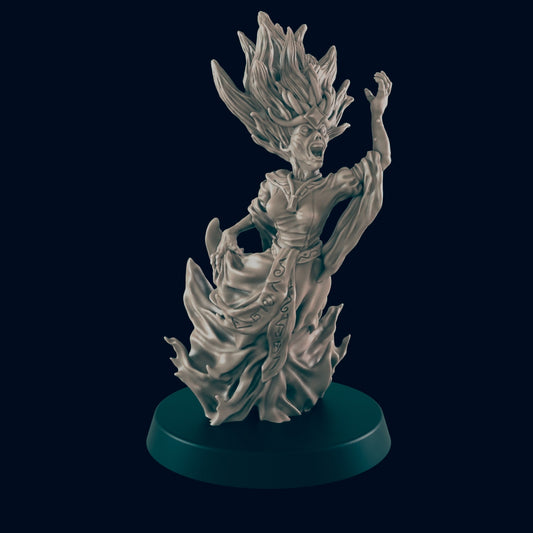 A grey miniature witch with flaming hair screams with one arm raised. She stands in a sculpted flame skirt on a round, dark base.
