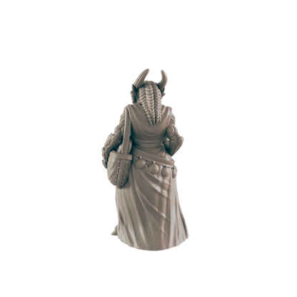 A miniature figurine of a horned, robed female figure stands with a satchel, viewed from behind against a dark background.