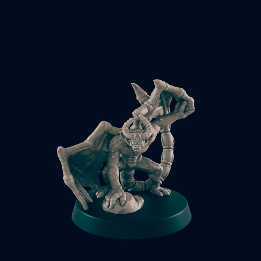 A demonic miniature figure, crouching and gripping a rock, is displayed on a circular base against a dark background.