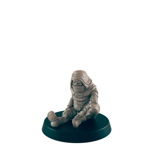 A small, hooded figurine sits on a dark circular base.  It appears to be made of light brown clay or resin. The figurine is in a seated position with its legs crossed.