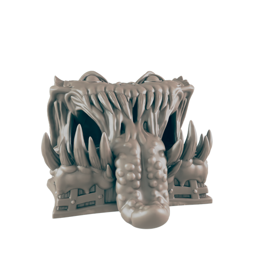 A monstrous, gray creature head, with a large tongue protruding, sits on a base.  Its mouth is open, revealing numerous sharp teeth.