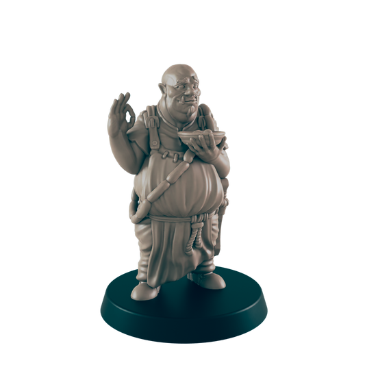 A stout, sculpted figure of a cook holds a bowl, gesturing with the other hand;  the figurine is displayed on a dark circular base.
