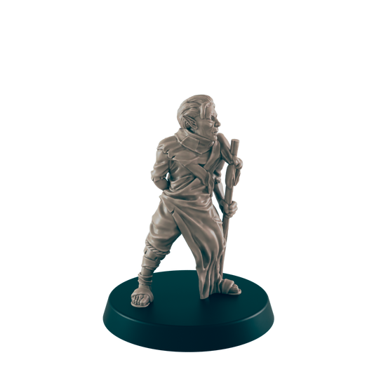 A miniature figurine of a robed humanoid stands holding a staff.  The figure is light beige, positioned on a dark circular base.