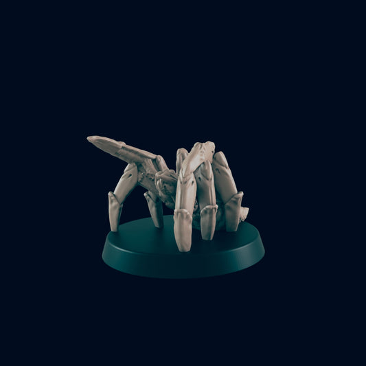 A mechanical spider miniature stands on a dark green base. The model is gray and looks like it is made of bone or ceramic in a dark, solid color environment.
